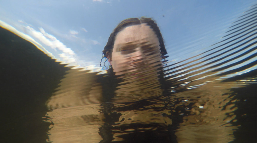Self-portrait taken from underwater of the artist, face obscured by ripples