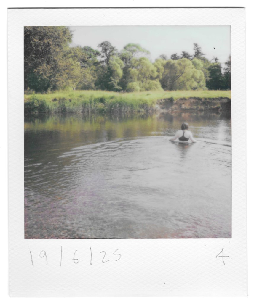 a polaroid photo of someone chest-deep in a calm river, facing away from the camera